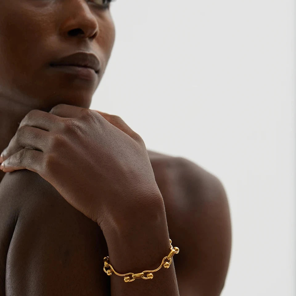 Halsband och armband set i guld med ett armband som placerar sig på en mänsklig handled lutandes mot ett knä