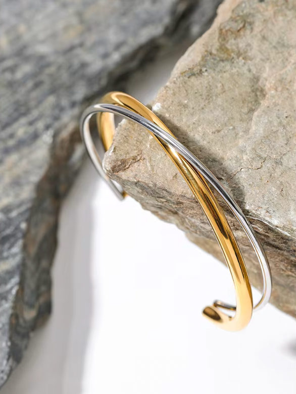 Armband i guld och silver som lutar sig mot en grå sten, elegant och stilren designat