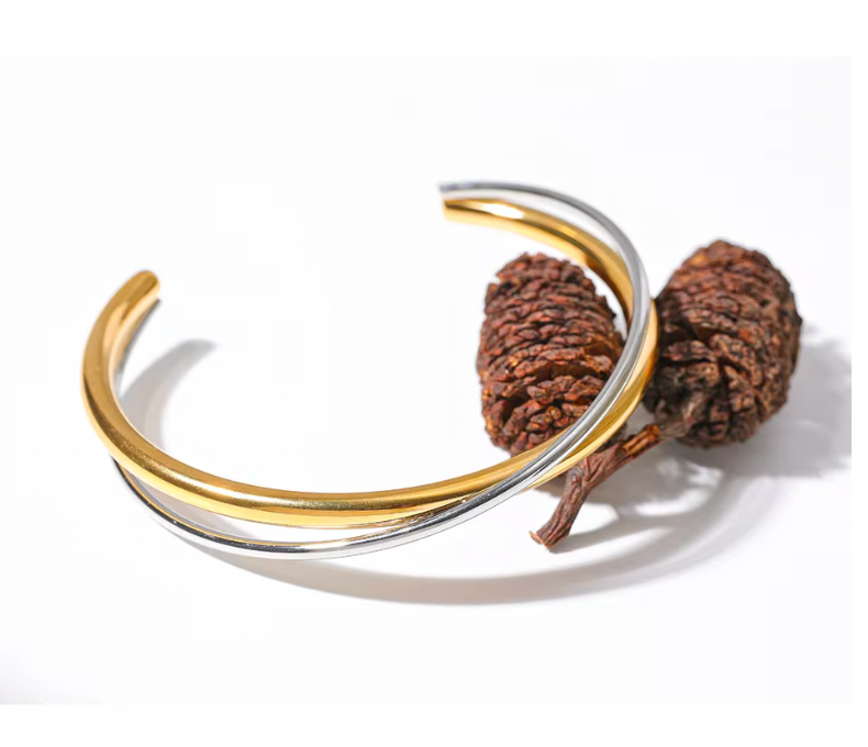 Armband i guld och silver som ligger på bruna kottar, elegant och stilrent designat.