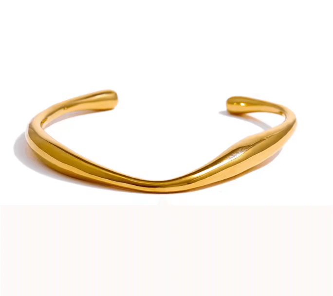 Armband i guld med en öppen design liggandes på en vit bakgrund 