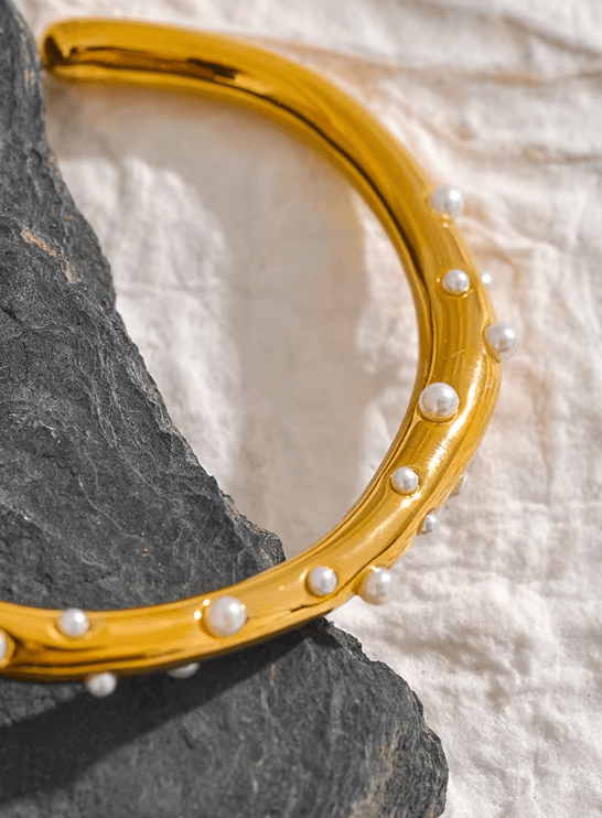 Armband i guld med kristaller och pärlor, elegant och stilrent designat, stilfullt placerat på en svart sten.